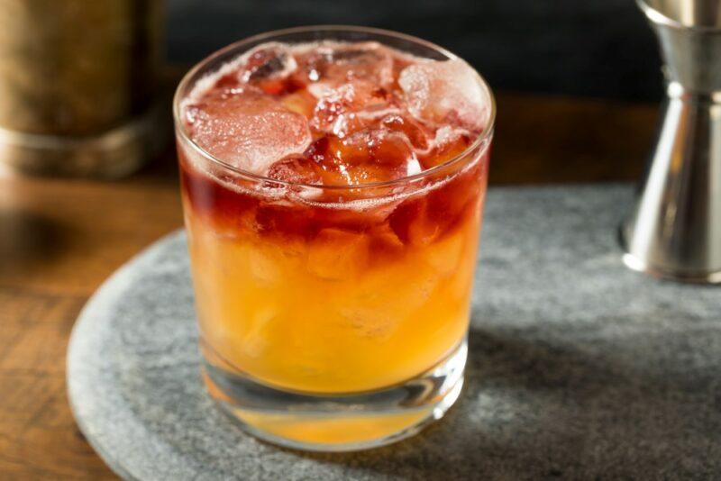 A single glass on a board with a New York sour cocktail with ice, next to a cocktail jigger