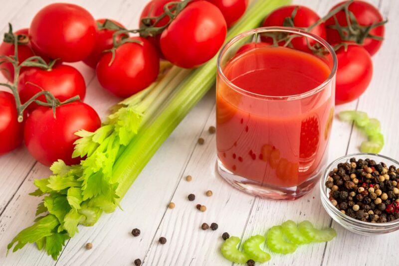 A cocktail made with tomatoes, next to tomatoes, celery, and pepper corns