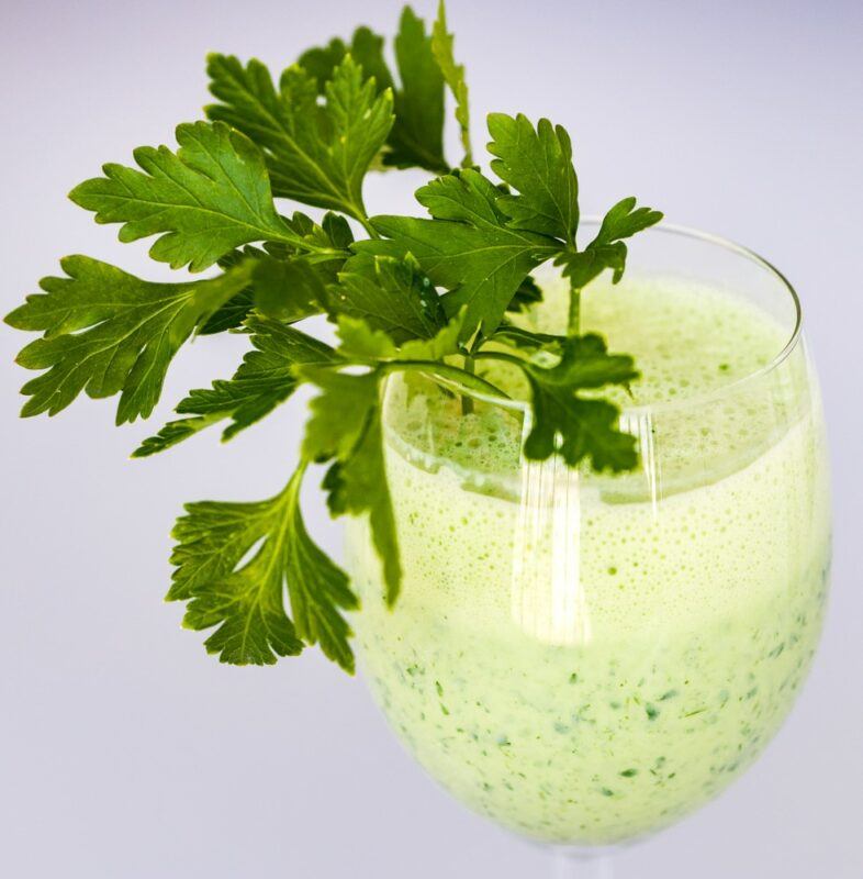 A glass on a gray table filled with a parsley juice and parsnip juice cocktail