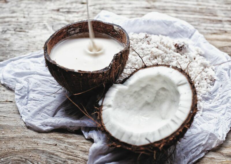 A coconut shell that's being filled with coconut milk and half of a coconut