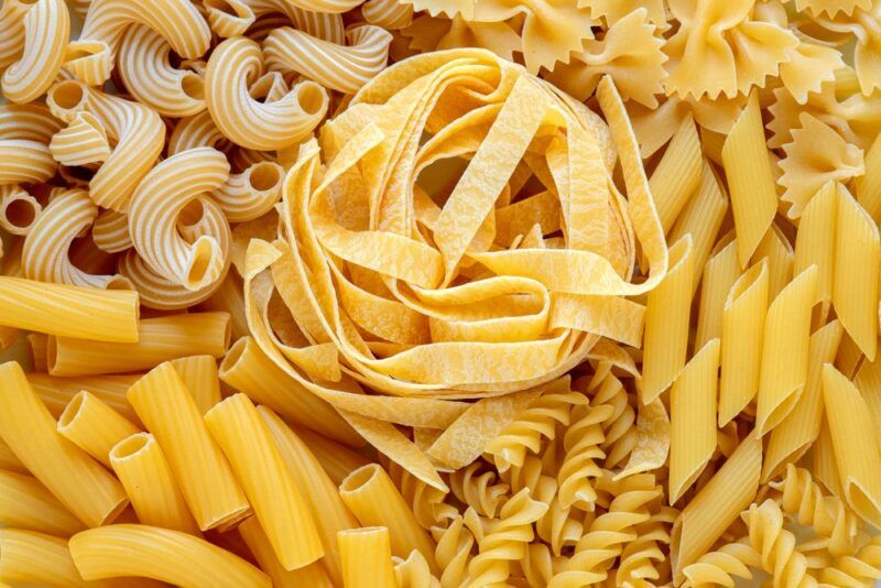 Many types of uncooked pasta on a table, including spiral pasta and fresh egg pasta.