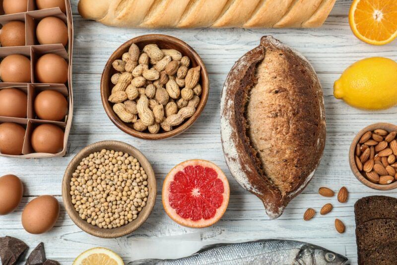 A white table where various allergy causing foods have been laid out, including eggs, soy, peanuts, grapefruit, bread, and almonds.