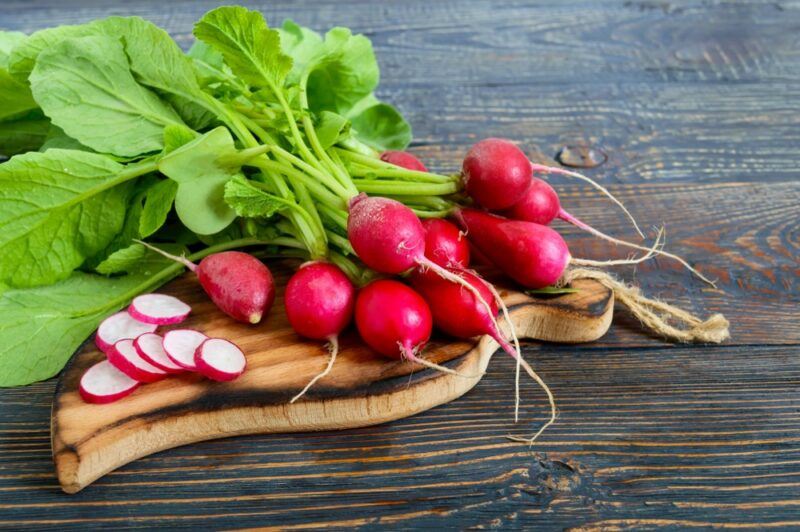 A wooden table with a board holding fresh radishes and a few radish slices