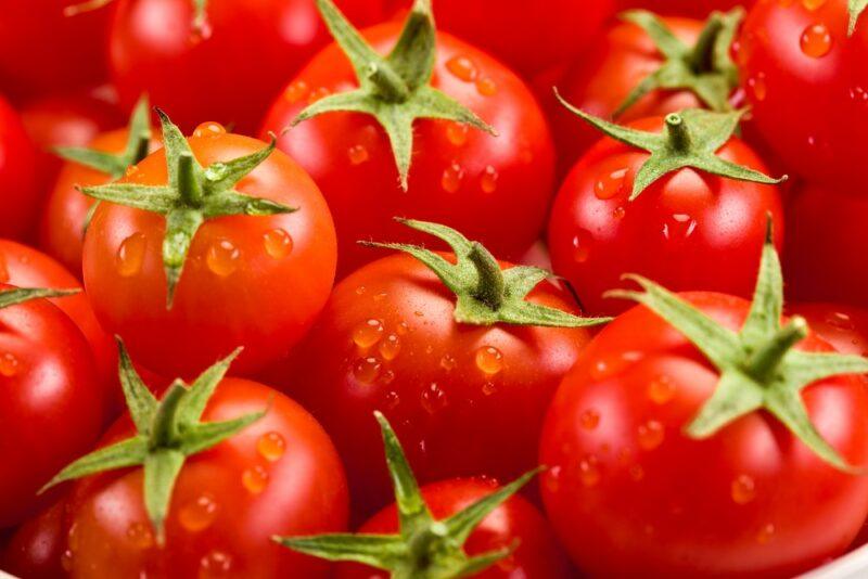 Many fresh tomatoes, each with a green cap and water droplets.