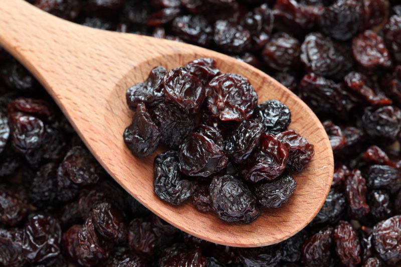 A collection of raisins with more raisins on a wooden spoon overtop