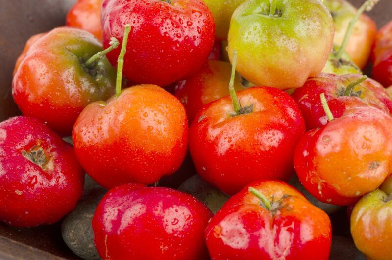 Fresh bright Barbados cherries in a pile. A few are green or partly yellow, rather than red