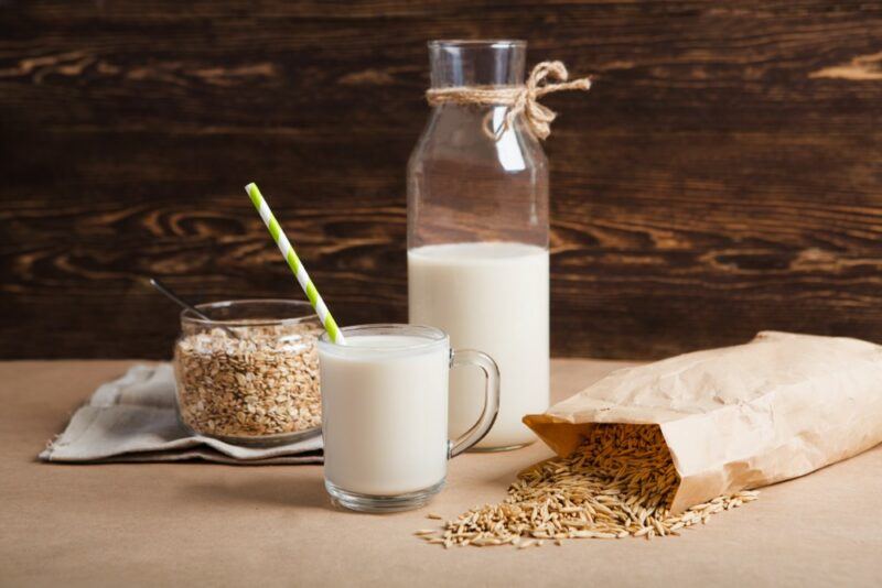 A bottle of oat milk and a small glass of oat milk near a jar of oats and a bag of oats