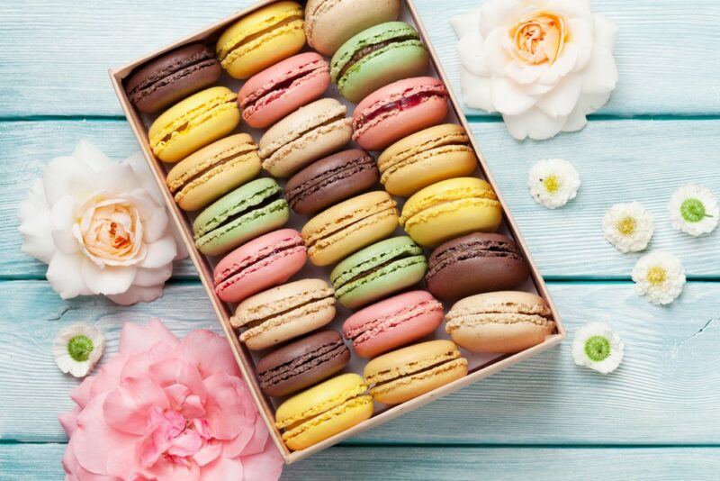 A container with many different colored macarons on a light blue table