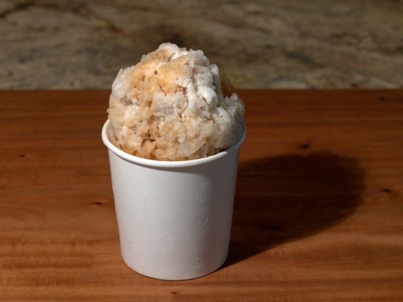 A tall paper cup containing a root beer float snow cone