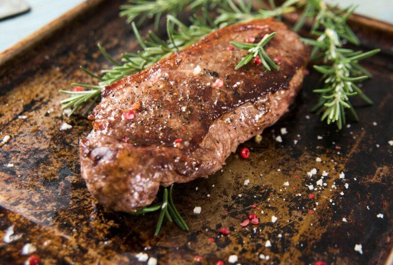 A wooden board with fresh sprigs of rosemary, a New York strip steak and plenty of salt