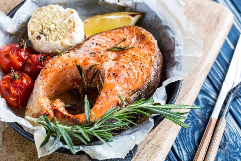 A dish with baking paper, baked salmon, garlic and herbs