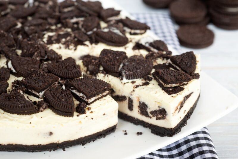 A cookies and cream cheesecake with broken Oreos on top, on a blue and white cloth