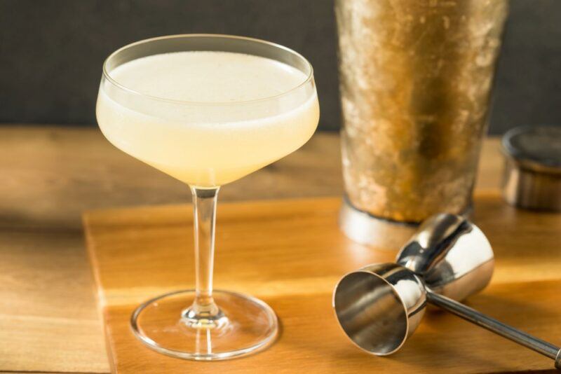 A corpse reviver cocktail on a wooden board next to a glass and a cocktail measure