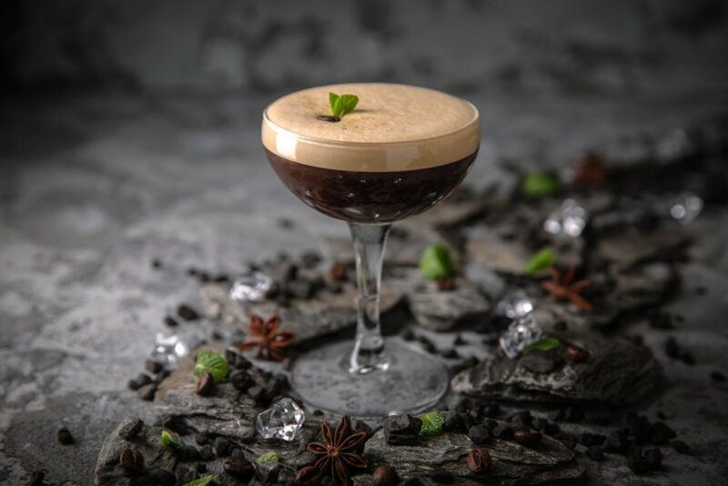 A coupe glass containing a drunken leprechaun cocktail, garnished with a small leaf, surrounded by chocolate