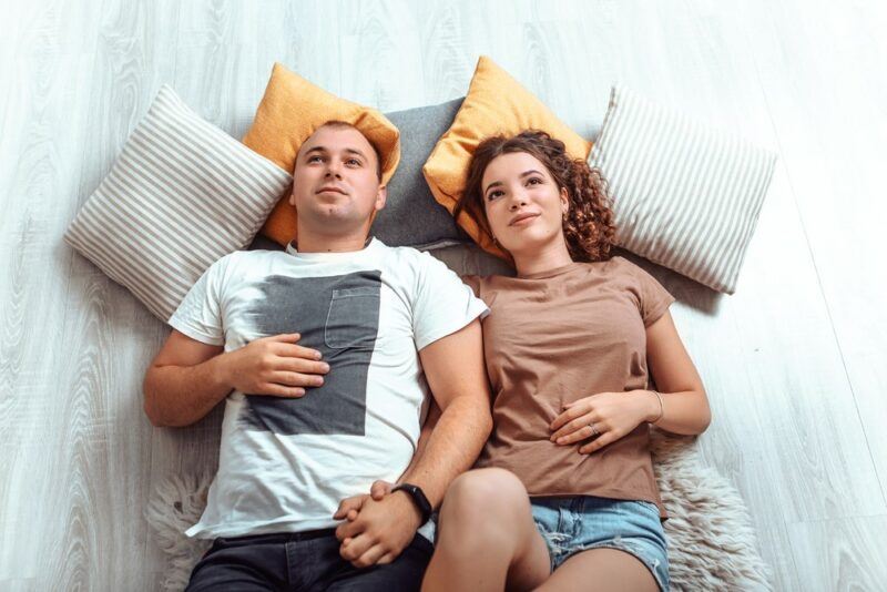 A young couple lying on the floor with cushions, looking at how to sleep on the floor