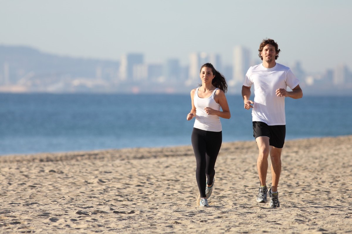 Runner of the Month Clubs - A couple running on the beach with the bay and city skyline in the background with blue hazy skies 