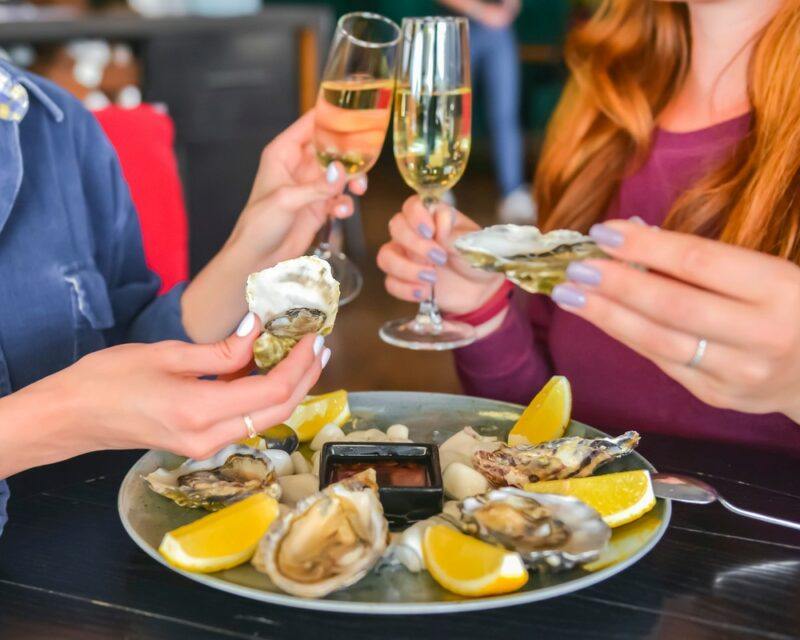 A group of people eating oysters while holding glasses of wine