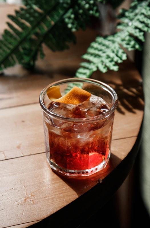 A cranberry old fashioned cocktail on the floor next to some plant fronds