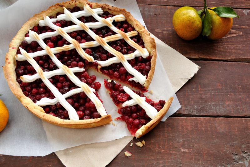 A cranberry pie with meringue lattice on pieces of paper with one piece of pie cut out of it