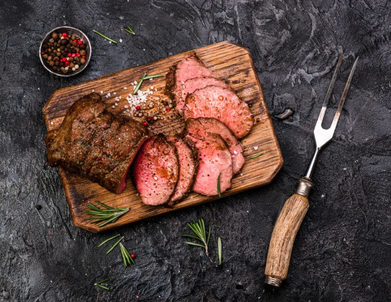 A wooden board with sliced rare beef on a black background