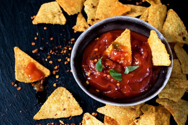 A black table with tortilla chips and a bowl of salsa or sauce