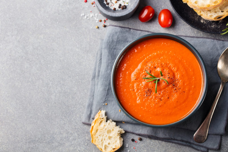 A black bowl that contains bright red soup on a gray or blue cloth