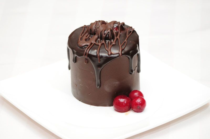 A tall dark chocolate mousse dessert on a white plate next to three red berries