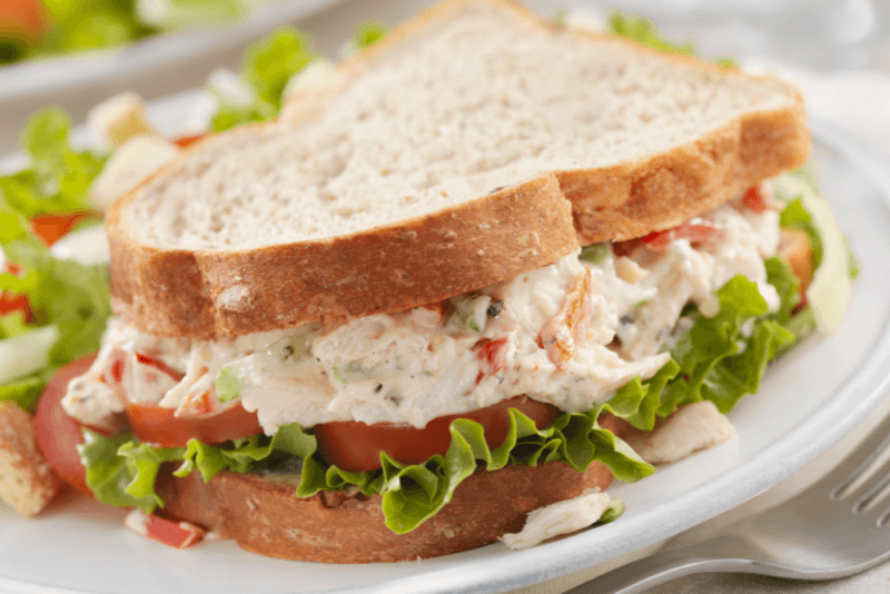 A crack chicken sandwich on white bread, with lettuce and tomatoes.