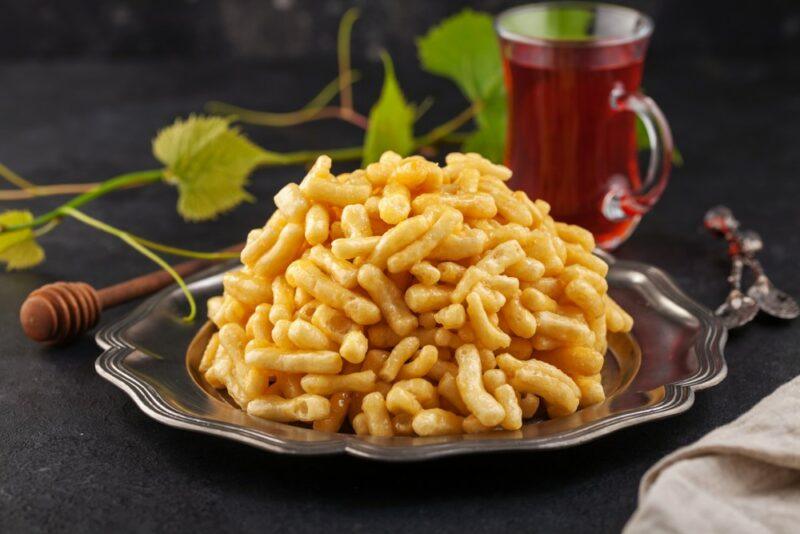 A dark bowl with a fried dessert called chak chak, with a mug of drink in the background