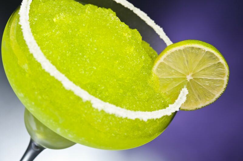 A close up image of a slushie dew garita cocktail rimmed with salt and a slice of lemon