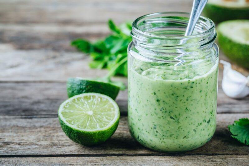 A glass jar containing a dip or dressing made using cilantro on a wooden board