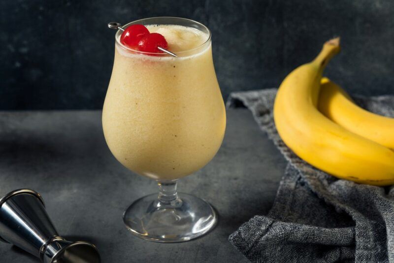 A glass containing a dirty banana cocktail, next to fresh bananas