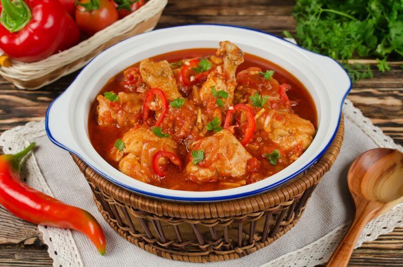 A deep white and blue dish that's filled with a chicken soup or stew called pollo guisado