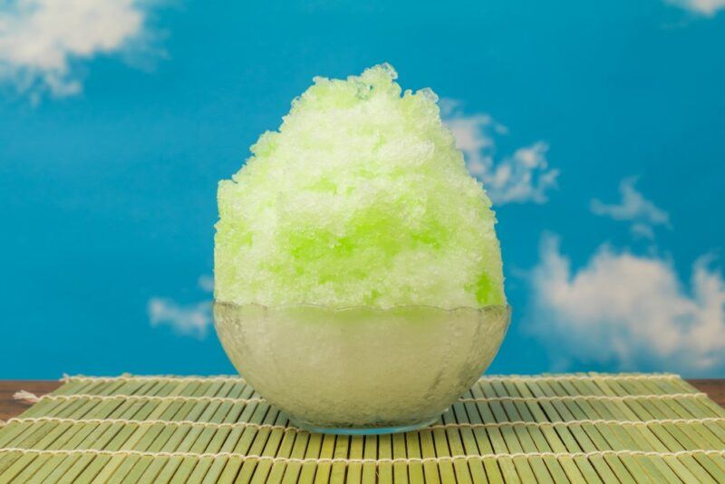 A bowl with a key lime snow cone on a mat against clouds in the background