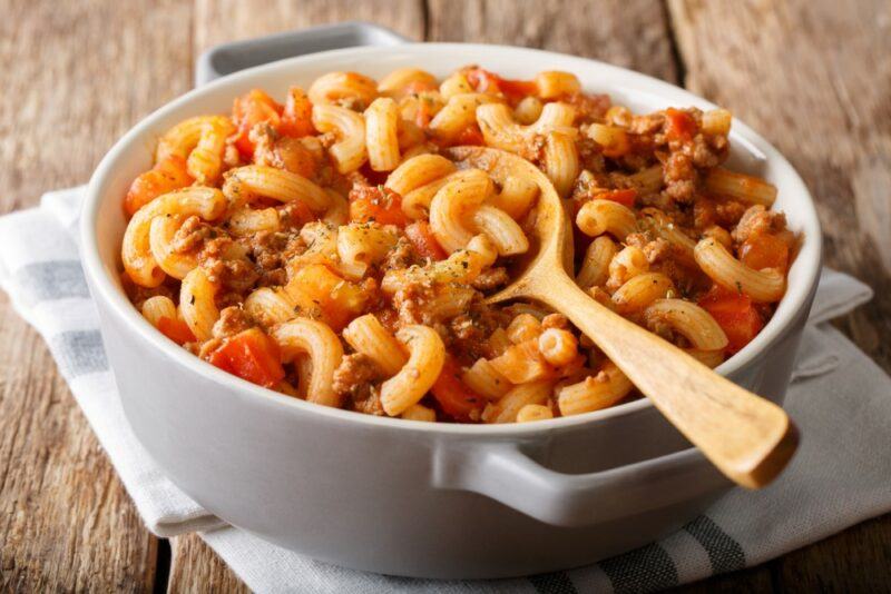 A large white dish containing macaroni and ground beef. with a wooden spoon