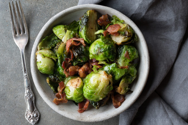 A white dish of Brussels sprouts with bacon