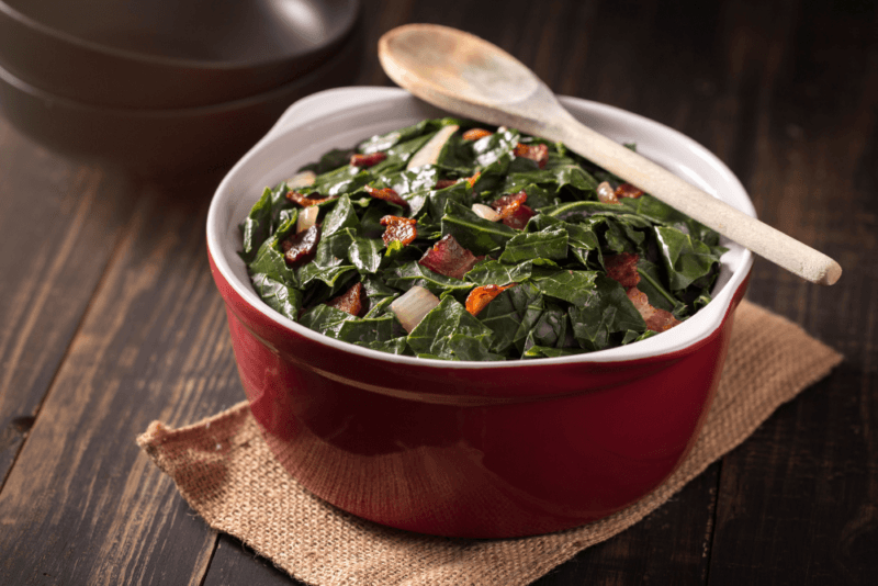 A red or brown dish with Southern collard greens ad a wooden spoon