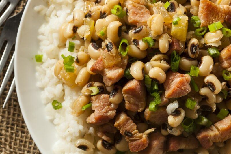 A large white plate with cooked rice, black eyed peas, and bacon