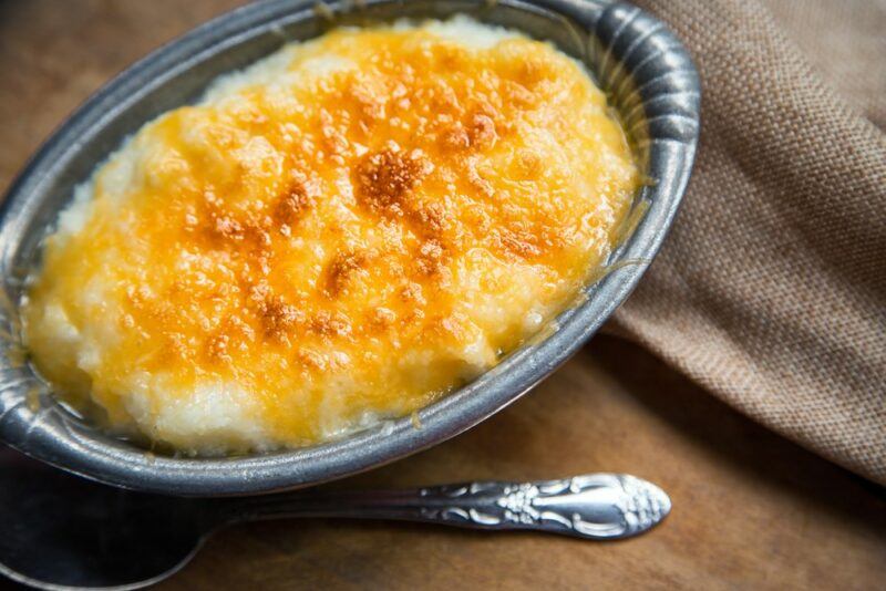 An oval dish of grits that are covered in cheese, with a spoon underneath