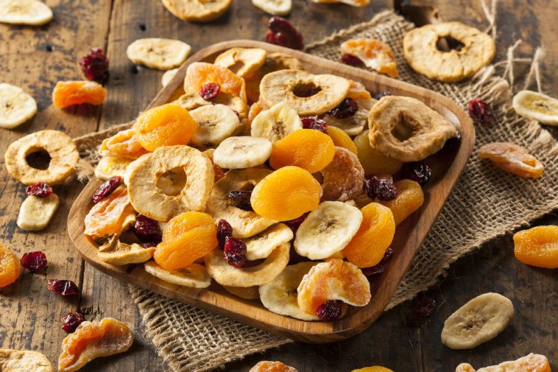 A brown dish of dried fruit and more scattered on a wooden table