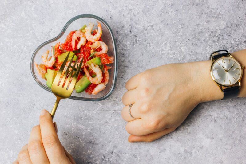 A grey table with a heart shaped dish of food, a person's hand and a watch