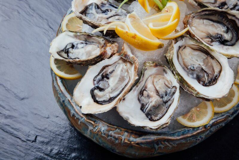 A dish of raw oysters with lemon wedges on a gray table