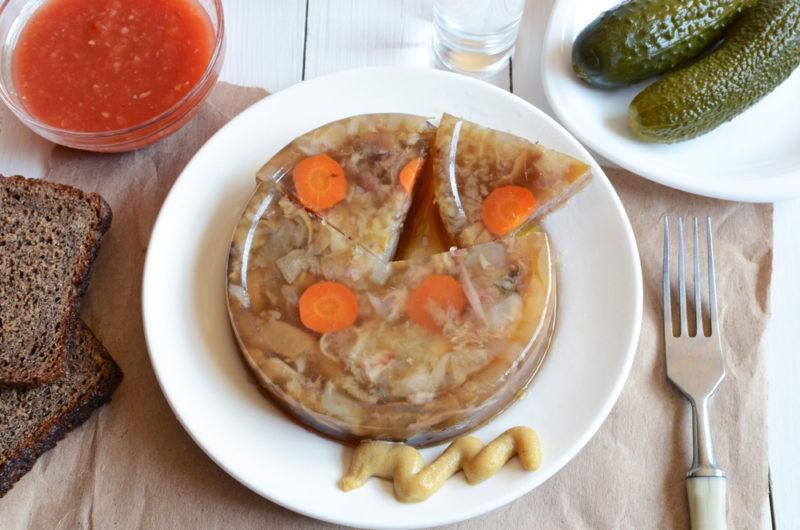 A white plate with jelly-like servings of plov and a little mustard, next to pickles and some type of sauce