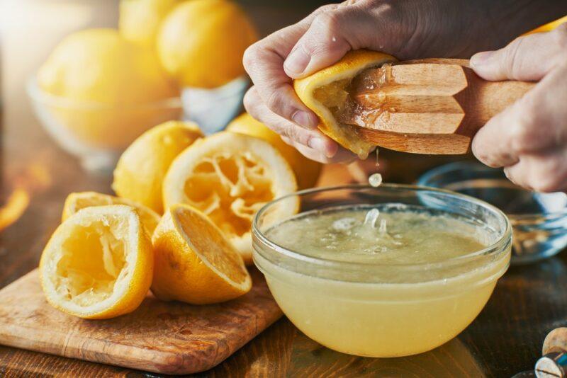 Someone using a hand tool to juice a lemon, with empty lemon halves next to it