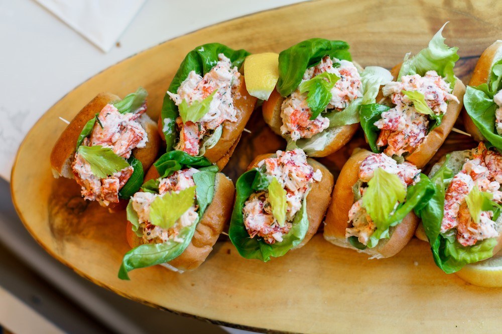 A wooden board with small freshly made lobster rolls