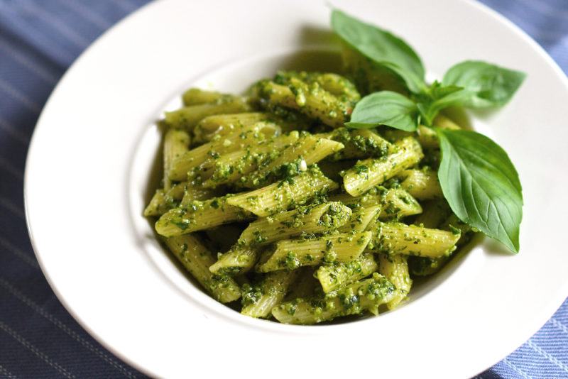 A large white dish of pesto pasta with basil leaves