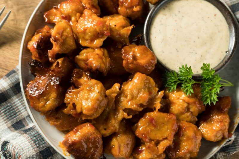 A dish of plant-based chicken nuggets, half surrounding a small container of dip