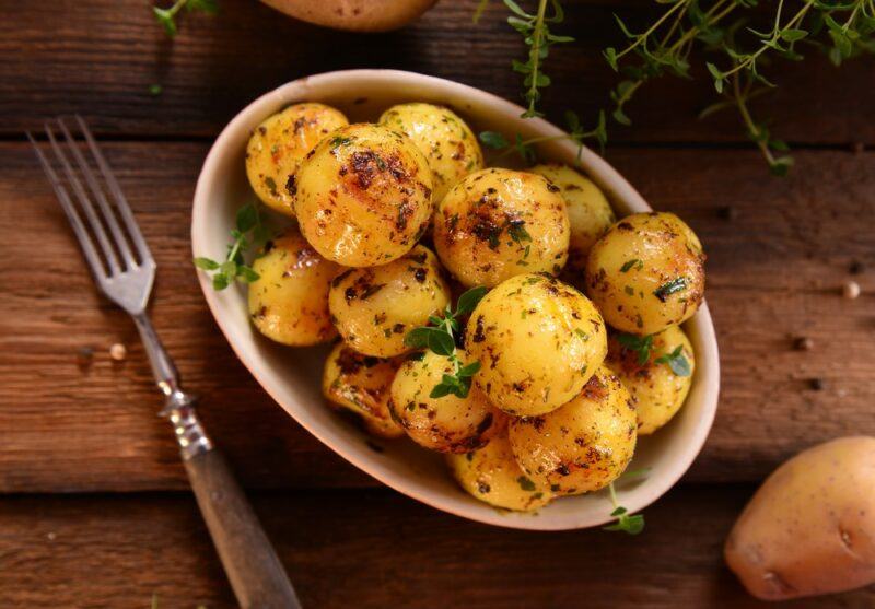 A large dish filled with roasted new potatoes next to a fork on a wooden table