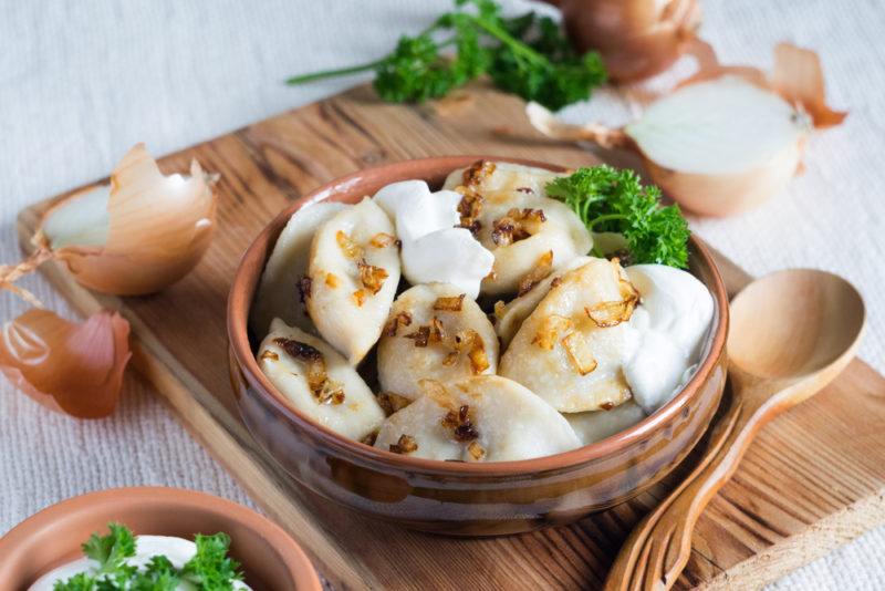 A brown dish of vareniki next to a wooden spoon on a wooden board