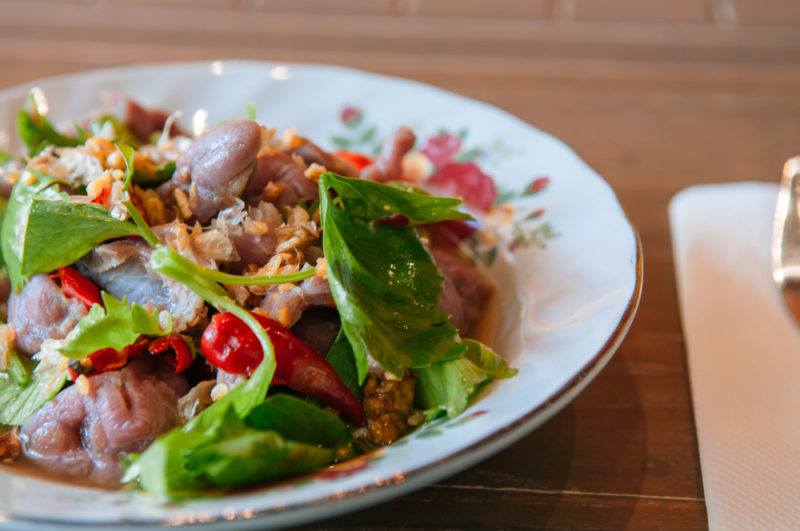 A white bowl with yum nua, which includes fried beef and greens